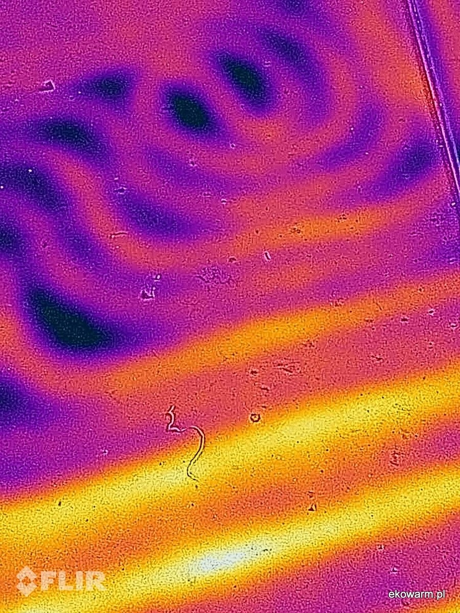 Termowizyjne zdjęcie rozkładu temperatury na powierzchni, ukazujące gradient od fioletu (chłodniej) do żółci i bieli (cieplej), z widocznym logo FLIR w rogu.