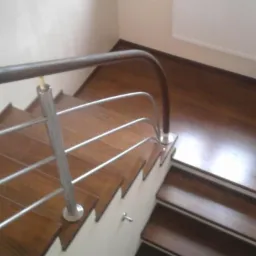 Widok z góry na brązowe schody z drewnianymi stopniami i metalową balustradą z ciemnobrązową poręczą, zakończoną złotym elementem.