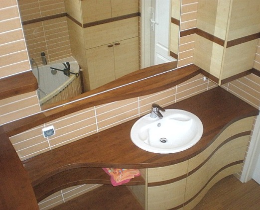 Nowoczesna aranżacja łazienki z umywalką wpuszczoną w drewniany blat o falistym kształcie, dopasowana kolorystycznie do szafek i płytek w odcieniach beżu i brązu.