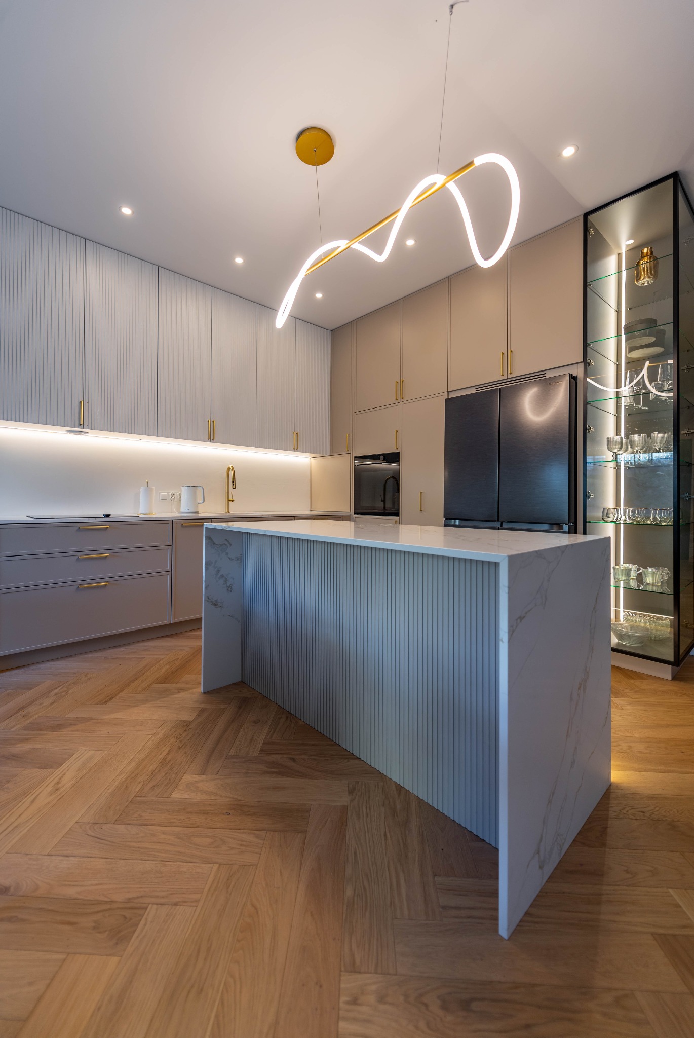 Nowoczesna kuchnia z wyspą wykończoną marmurem, drewnianą podłogą w jodełkę i oświetleniem LED