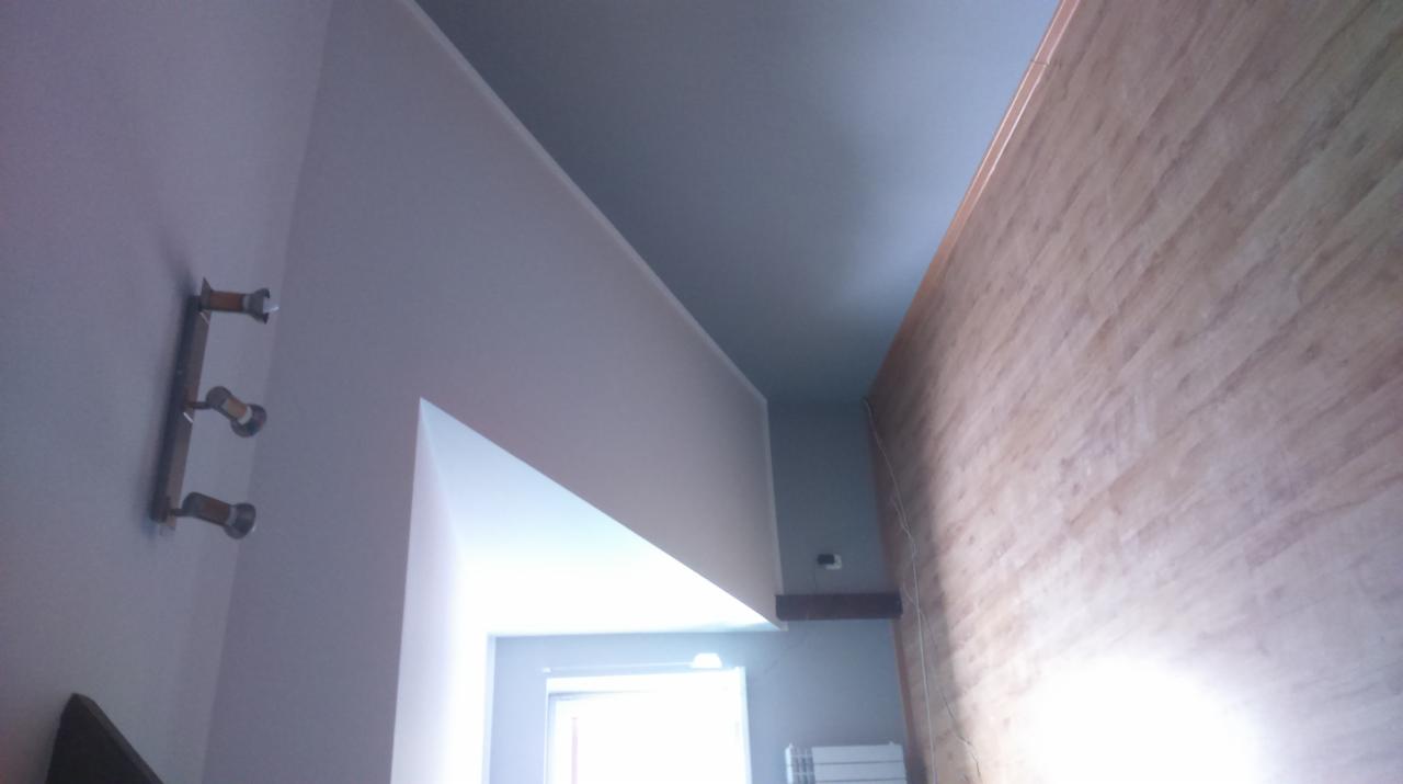 Pomieszczenie po malowaniu, z pomalowanym sufitem na szaro, drewnianą ścianą i grzejnikiem pod oknem.