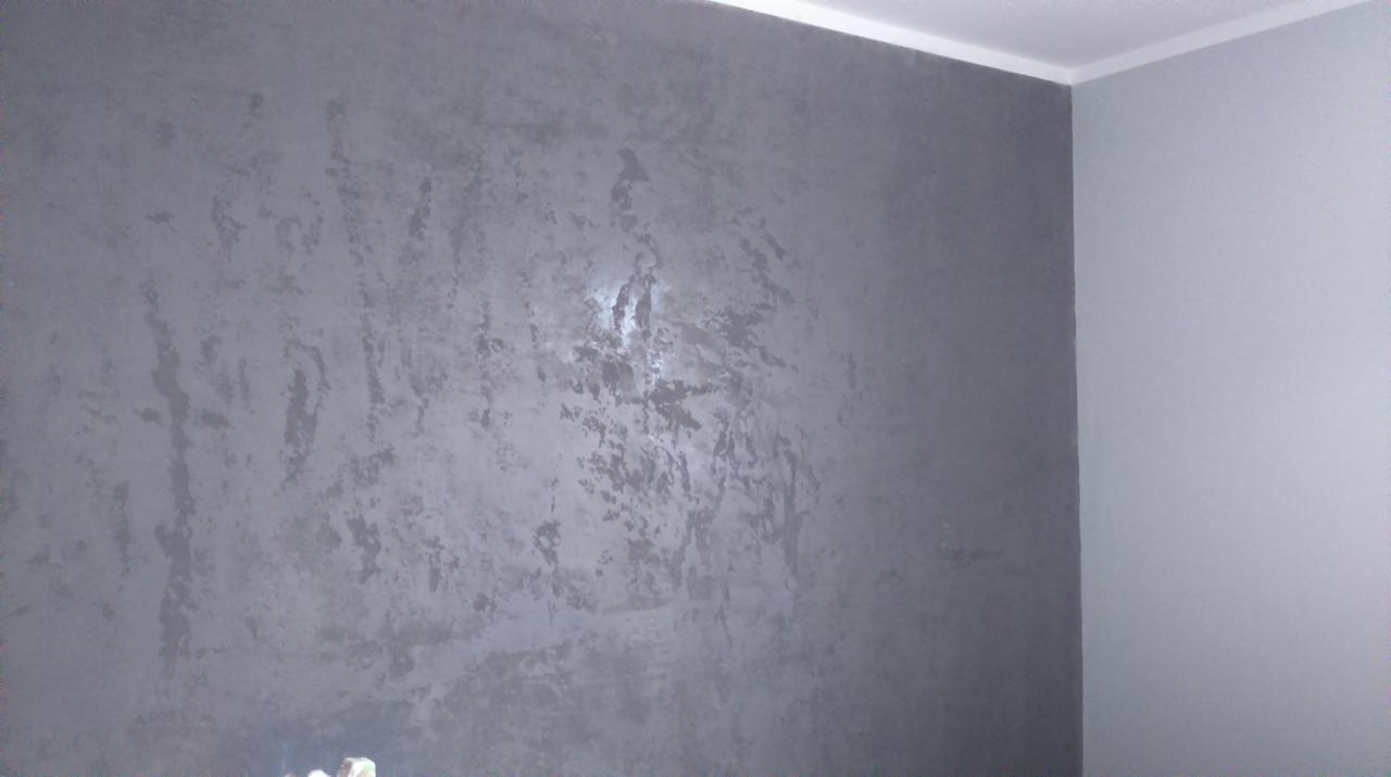 Ściana w pokoju pokryta dekoracyjną, szarą gładzią z efektem przetarć, widoczny fragment sufitu z listwą przypodłogową.