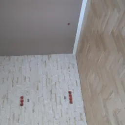 Wykończone wnętrze: ściana z dekoracyjnej okładziny imitującej kamień, świeżo ułożony parkiet w jodełkę francuską i pomalowany sufit w odcieniach beżu, widoczne gniazdka elektryczne.