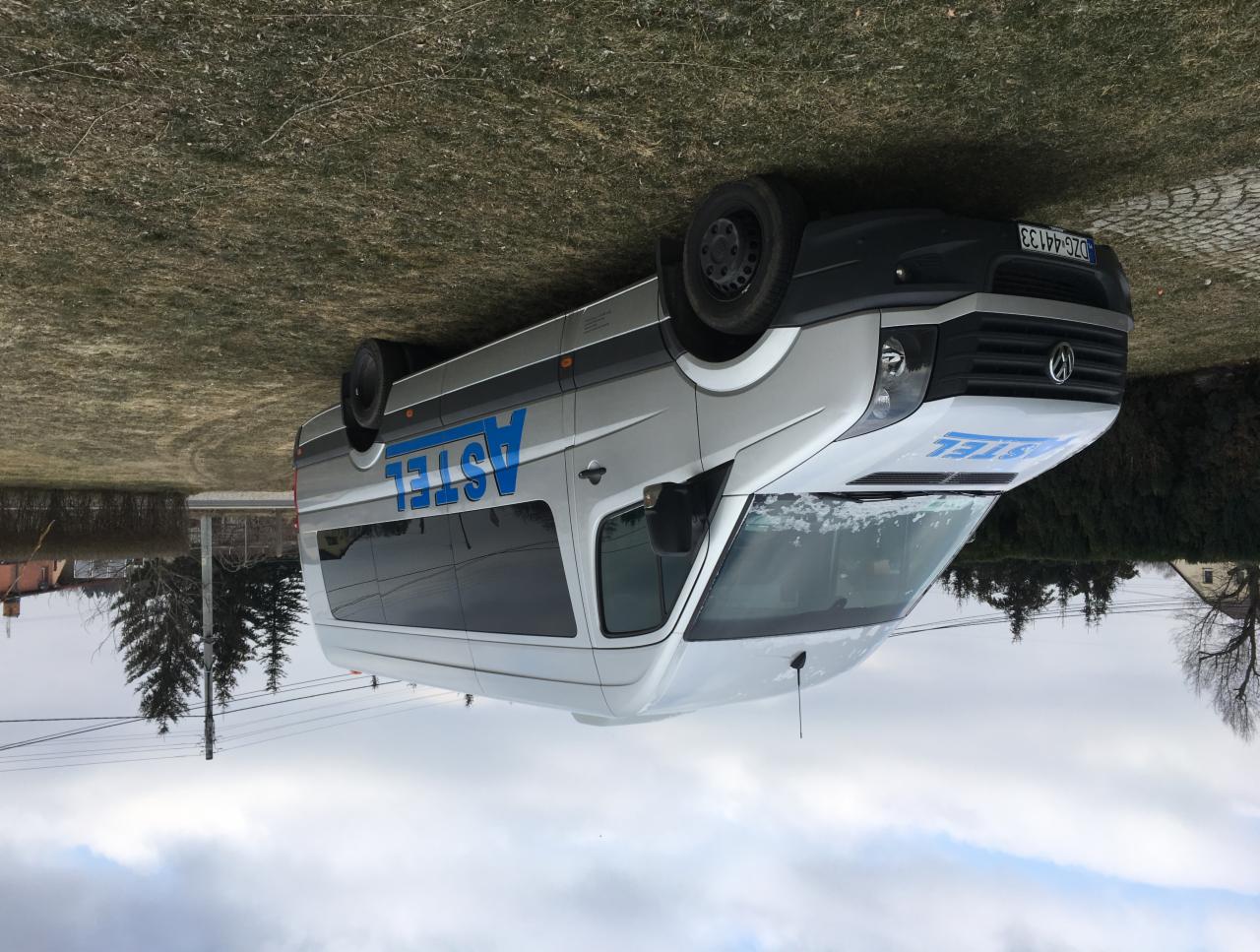 Biały bus z niebieskim napisem 'ASTEL' na boku, zaparkowany na trawie, widoczny numer rejestracyjny DZG 44133.