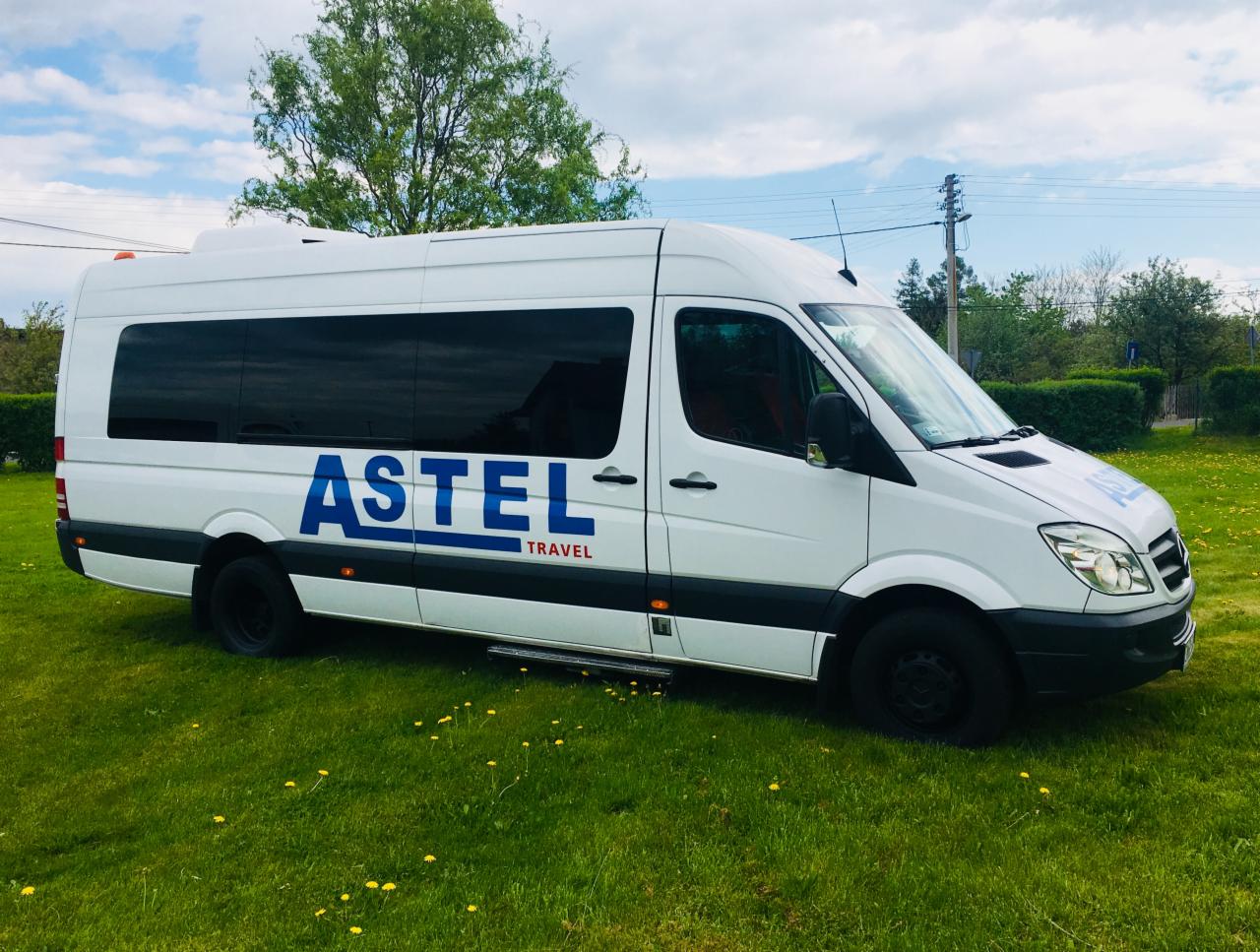 Biały bus marki Mercedes Sprinter z niebieskim napisem 'ASTEL TRAVEL' na zielonym trawniku, widoczne otwarte drzwi z wysuwanym stopniem.
