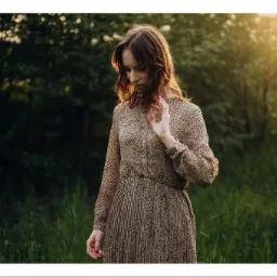 Portret kobiety w plenerze, w sukience w panterkę, z rozproszonym światłem słonecznym w tle.