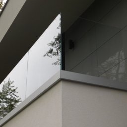 MGX Sp. z o.o. - Nowoczesna balustrada szklana na balkonie z widocznym odbiciem drzewa, minimalistyczny design.