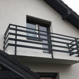 MGX Sp. z o.o. - Balkon z czarną, metalową balustradą z poziomych profili, zamontowaną do białej elewacji budynku z ciemną dachówką.