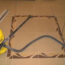 tomasz błasek - Beżowe płytki podłogowe z dekoracyjnym brązowym obramowaniem w trakcie czyszczenia odkurzaczem przemysłowym Karcher, obok listwa przypodłogowa.