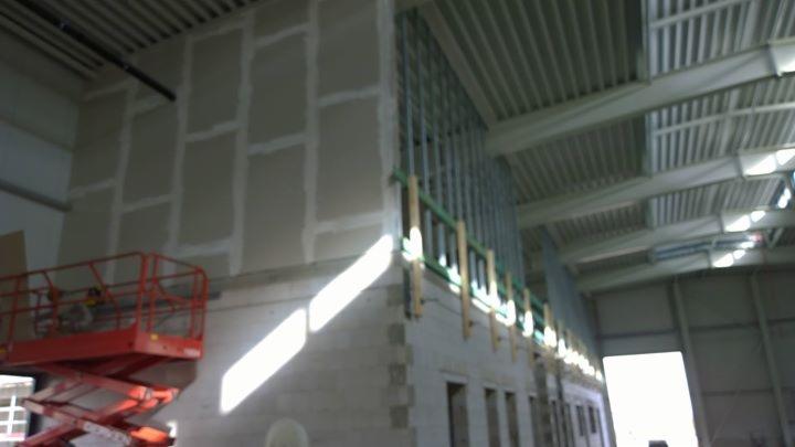 Wnętrze hali w trakcie prac wykończeniowych: szpachlowane ściany z płyt gipsowo-kartonowych, widoczna konstrukcja metalowa i podnośnik nożycowy.