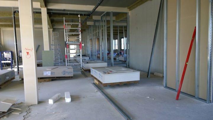 Wnętrze w trakcie szpachlowania: metalowe profile ścian działowych, płyty gipsowo-kartonowe na paletach, poziomica oparta o ścianę, drabina aluminiowa.