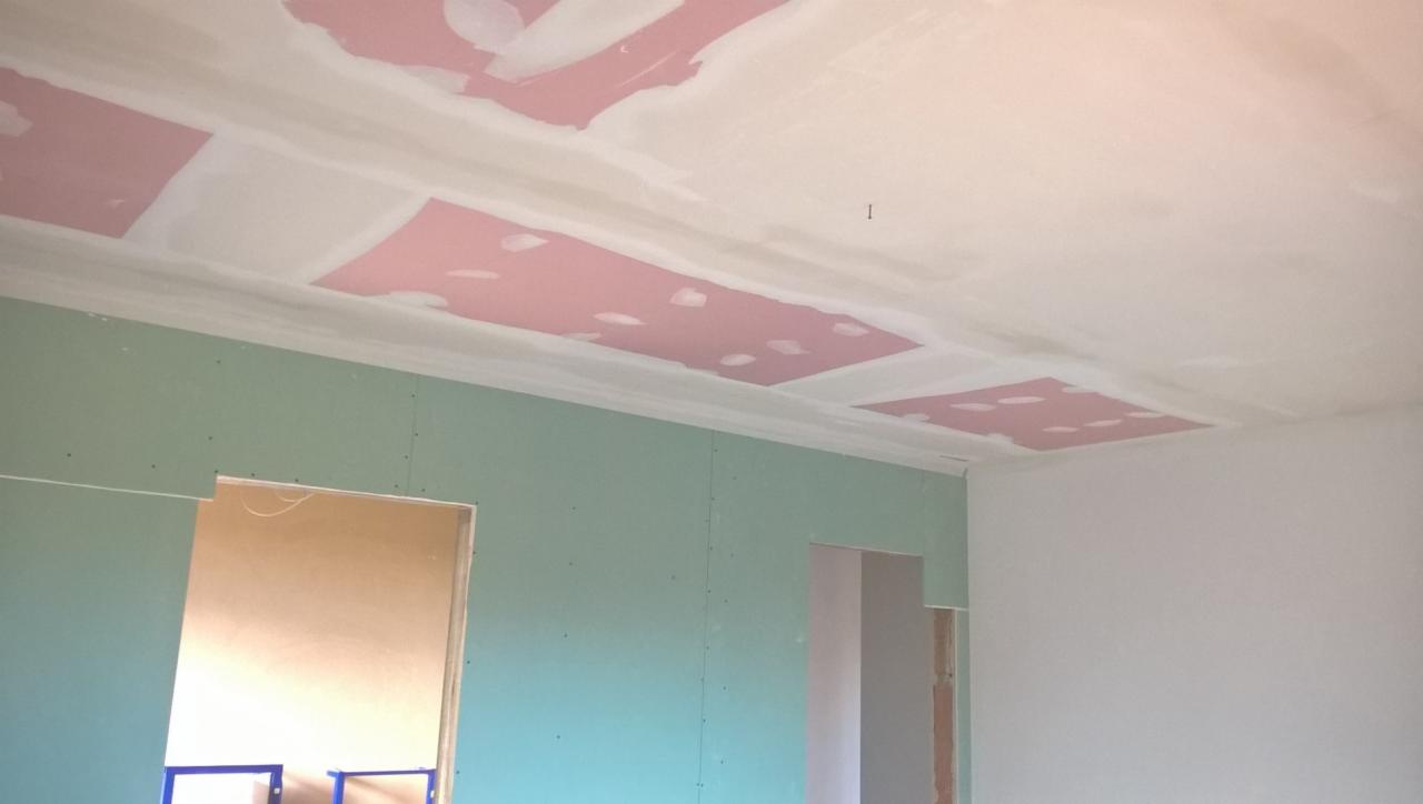 Wnętrze w trakcie remontu: ściany pokryte zielonymi płytami gipsowo-kartonowymi, sufit z widocznymi fragmentami różowych płyt i świeżo nałożoną warstwą szpachli, przygotowywany do dalszych prac...