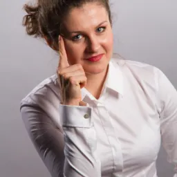 Portret kobiety w białej koszuli z mankietami na spinki, zamyślona mina, palec wskazujący przy skroni.