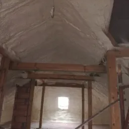 Poddasze domu ocieplone pianką PUR, widoczne drewniane elementy konstrukcyjne i małe okno na końcu pomieszczenia, na suficie wisi mała rybka.