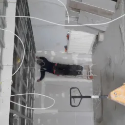 Pracownik leżący na wózku paletowym, prowadzący instalację kabli elektrycznych wewnątrz metalowej konstrukcji sufitu podwieszanego w surowym stanie.