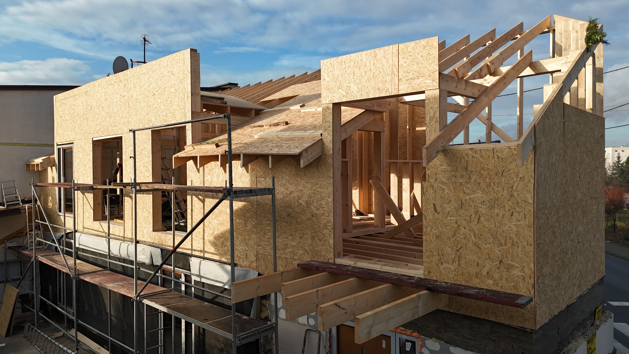 Budowa domu w stanie surowym otwartym z drewnianą konstrukcją szkieletową i płytami OSB, widok z rusztowania, błękitne niebo w tle.