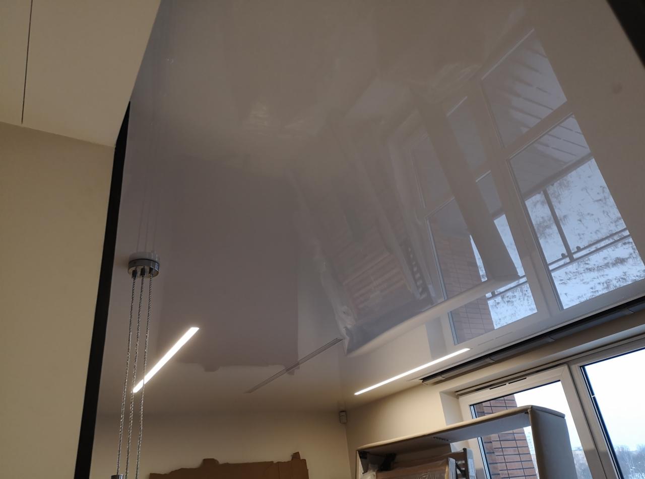 Błyszczący, szary sufit napinany z widocznymi liniami oświetleniowymi LED i odbiciem okna w powierzchni.