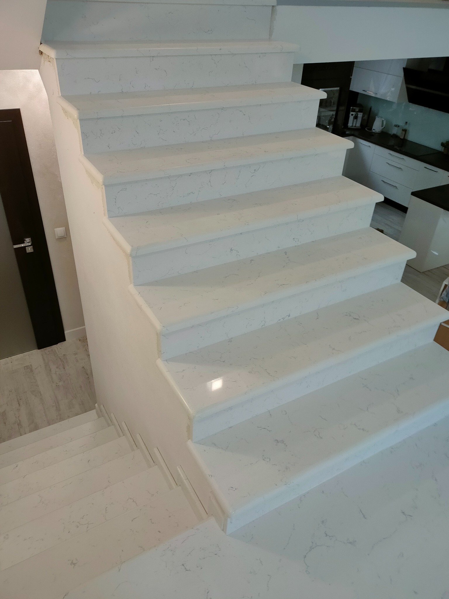 Jasne, marmurkowe schody wewnętrzne z widokiem na kuchnię w tle.