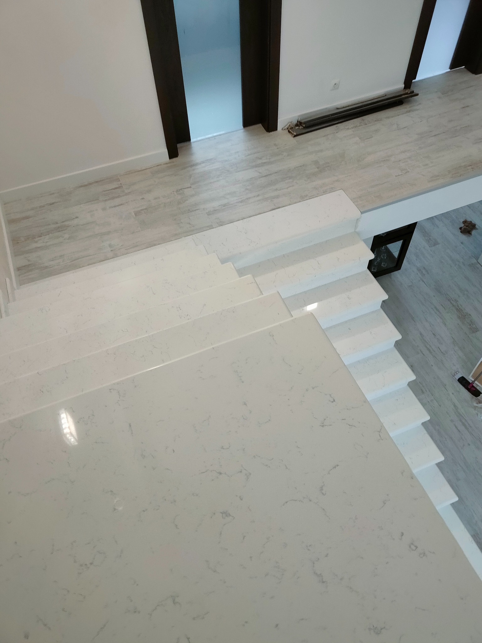 Białe schody kamienne z widocznym wzorem użylenia, widziane z góry, z fragmentem podłogi i drzwi w tle.