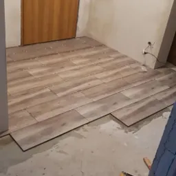 Układanie płytek podłogowych imitujących drewno w trakcie remontu, widoczna poziomica i paczka płytek.