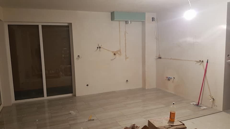 Wnętrze w trakcie prac remontowych: świeżo położona podłoga z płytek, ściany przygotowane pod instalacje elektryczne i hydrauliczne, widoczne kable i rury, przygotowany sufit podwieszany, mop...