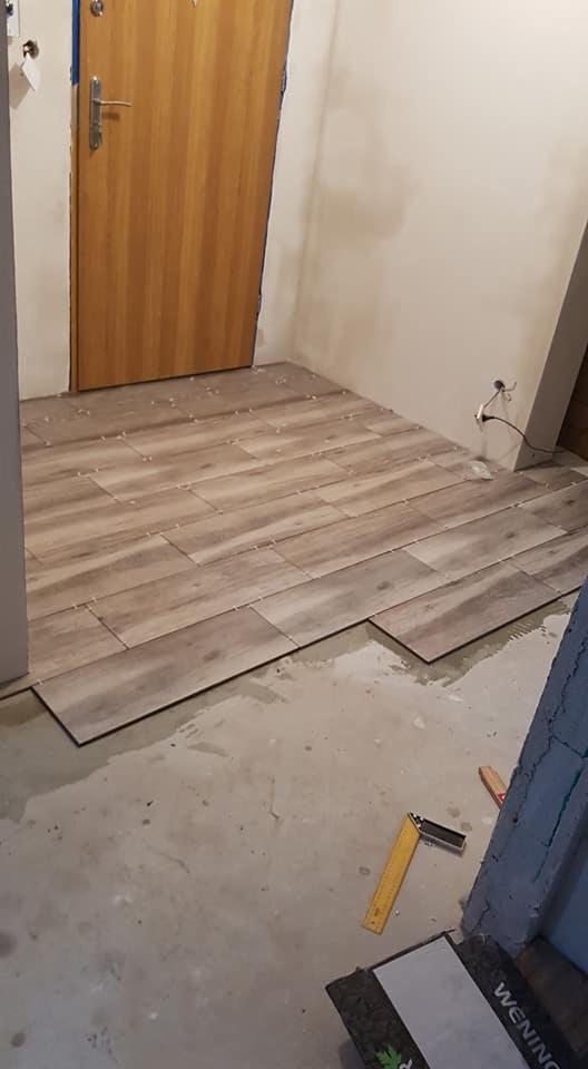 Układanie płytek podłogowych imitujących drewno w trakcie remontu, widoczna poziomica i paczka płytek.