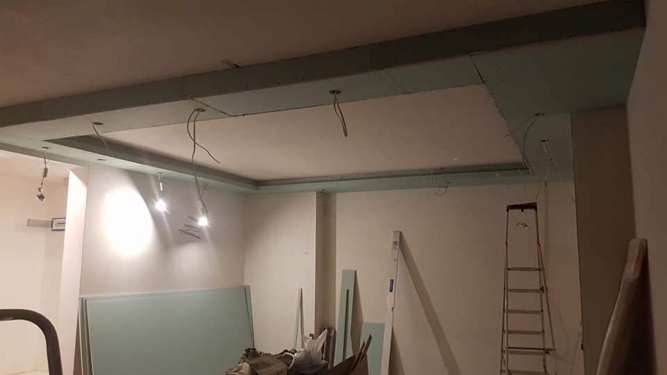 Sufit podwieszany z płyt gipsowo-kartonowych w trakcie montażu, widoczne kable oświetleniowe, drabina i płyty gotowe do użycia.
