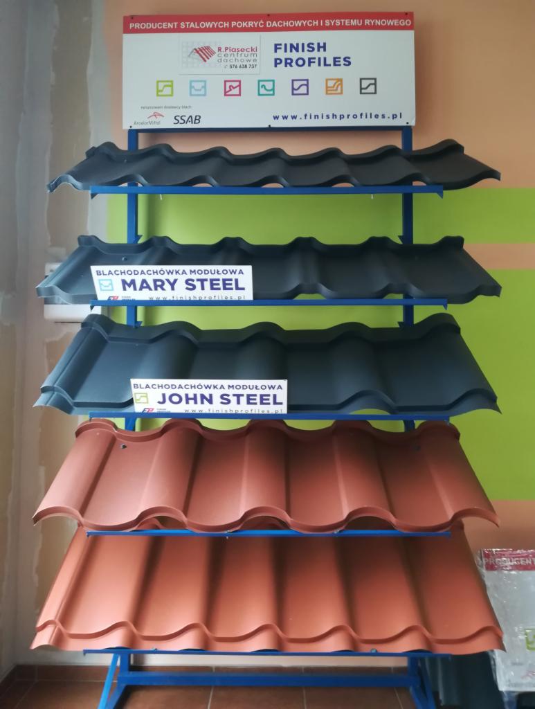 Ekspozycja różnych modeli blachodachówki modułowej na metalowym regale, prezentacja kolorów i wzorów, widoczny szyld producenta stalowych pokryć dachowych Finish Profiles.