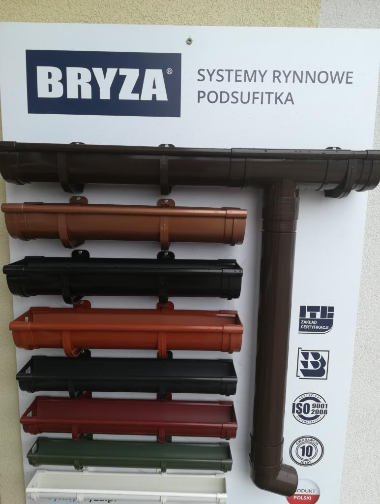Ekspozycja systemów rynnowych Bryza w różnych kolorach, z logiem producenta i certyfikatami jakości na białym tle.