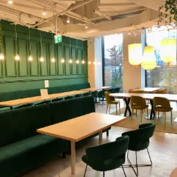 Wnętrze restauracji w Varso Tower z zielonymi tapicerowanymi ławami, drewnianymi stołami i wiszącymi lampami z abażurami, widok na miasto za oknem.