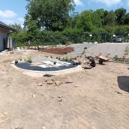 SPDE Serwis ogrodowy - Aranżacja terenu wokół domu: okrągła rabata z roślinami i żwirem na czarnej agrowłókninie, betonowe schody, pracownicy na placu budowy ogrodu.