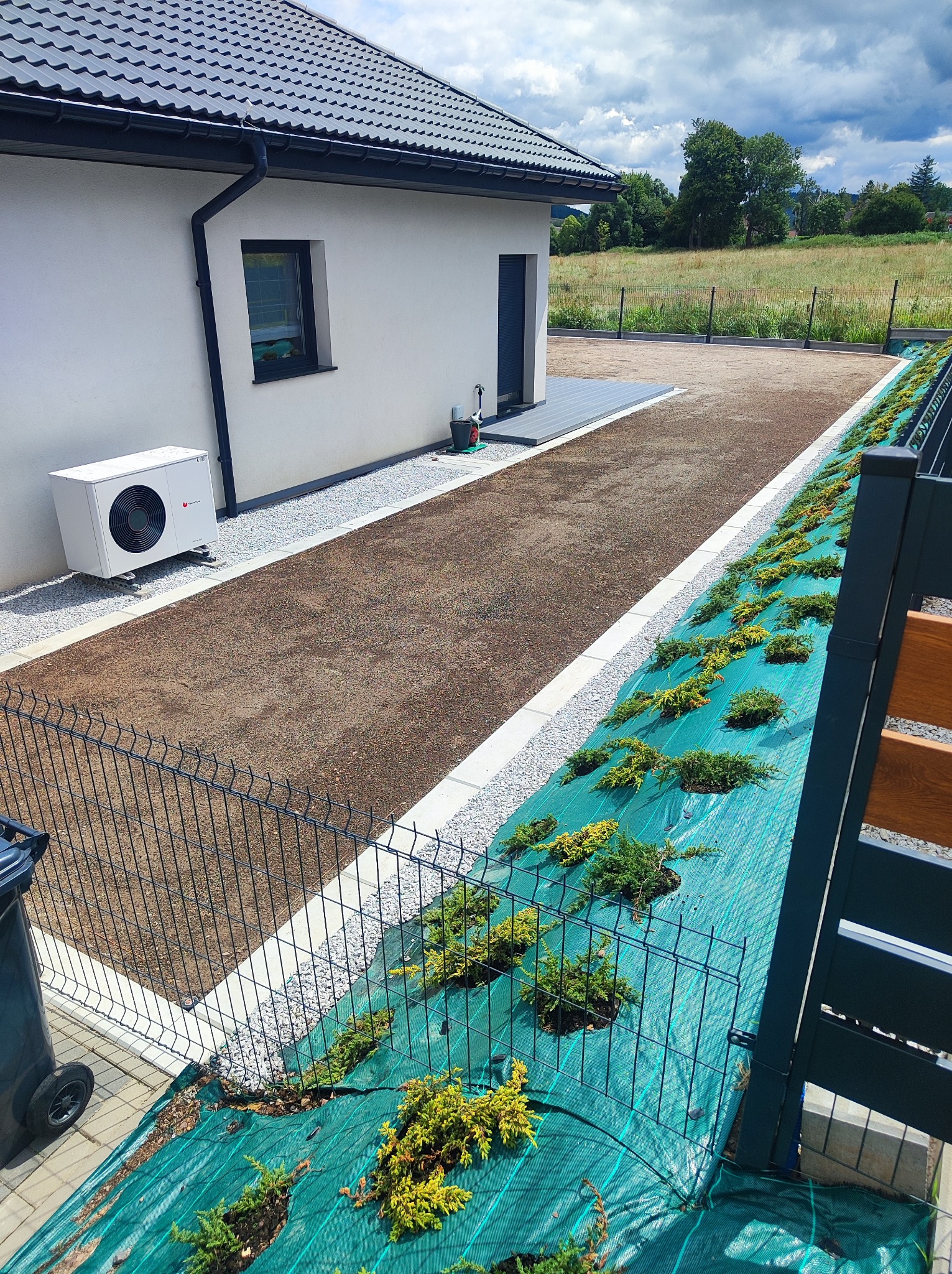 Przygotowanie terenu pod ogród w Wałbrzychu: wyrównana ziemia, obrzeża z kamienia, mata szkółkarska z nasadzeniami, nowoczesny budynek w tle.