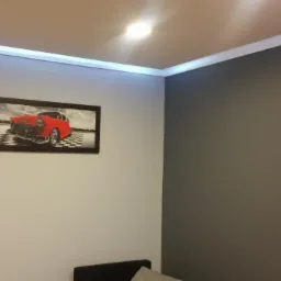 Pokój z pomalowanymi ścianami na szaro i biało, z oświetleniem LED przy suficie i obrazem czerwonego samochodu w czarnej ramie.