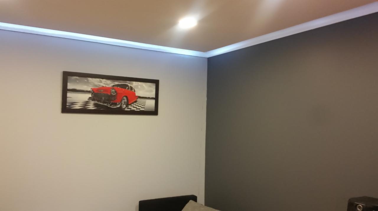 Pokój z pomalowanymi ścianami na szaro i biało, z oświetleniem LED przy suficie i obrazem czerwonego samochodu w czarnej ramie.