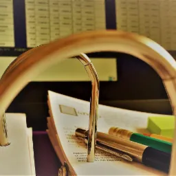 Otwarty segregator z dokumentami, długopisami i karteczkami samoprzylepnymi na biurku, w tle widoczny monitor z arkuszem kalkulacyjnym.