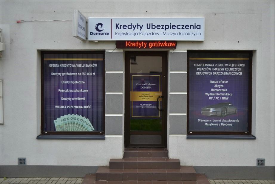 Fasada budynku Centrum Kredytów i Ubezpieczeń Domena z ofertami widocznymi na szybach: kredyty gotówkowe, hipoteczne, pożyczki, ubezpieczenia OC/AC/NNW oraz pomoc w rejestracji pojazdów.