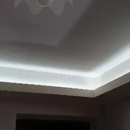 Wykończony sufit podwieszany z oświetleniem LED wzdłuż krawędzi, widoczne okno w dolnej części kadru.