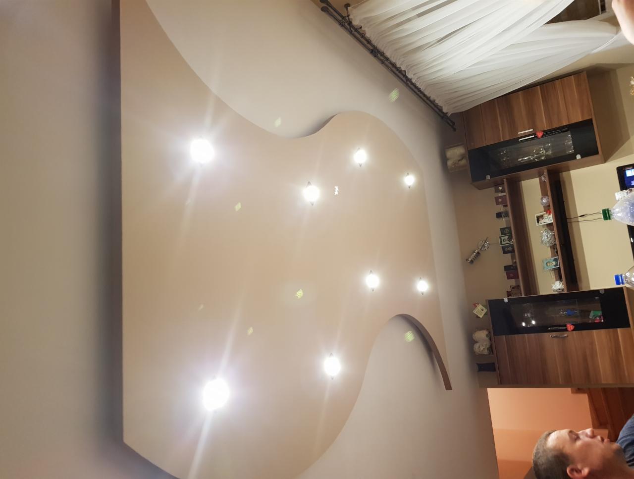 Nietypowy sufit podwieszany z oświetleniem punktowym w kształcie organicznym, widok z dołu, fragment mebli w tle.