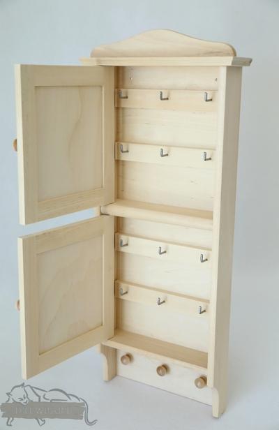 Otwarta, drewniana szafka na klucze z haczykami wewnątrz, widoczne trzy okrągłe uchwyty na dole.