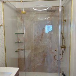TNS-Glass - Nowoczesna kabina prysznicowa z transparentnego szkła, złote okucia, marmurowe płytki w odcieniach beżu i różu, szklane półki. Eleganckie wykończenie łazienki.