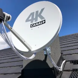Antena satelitarna 4K Canal+ zamontowana na kominie domu z widocznymi kablami koncentrycznymi i niebieskim niebem w tle.