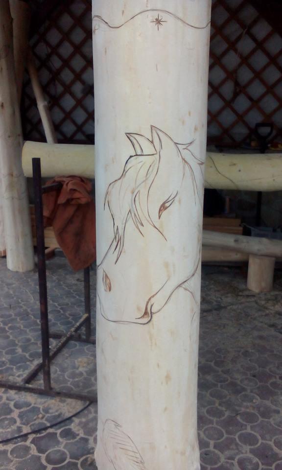 Surowy drewniany słup z wyrytym konturem głowy konia i gwiazdy, element dekoracyjny w trakcie tworzenia, widoczne ślady ołówka.