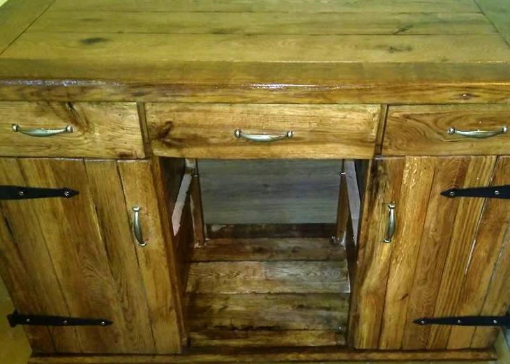 Rustykalna komoda z drewna z trzema szufladami i dwojgiem drzwi z czarnymi zawiasami, widoczne niedoskonałości i naturalny rysunek drewna.