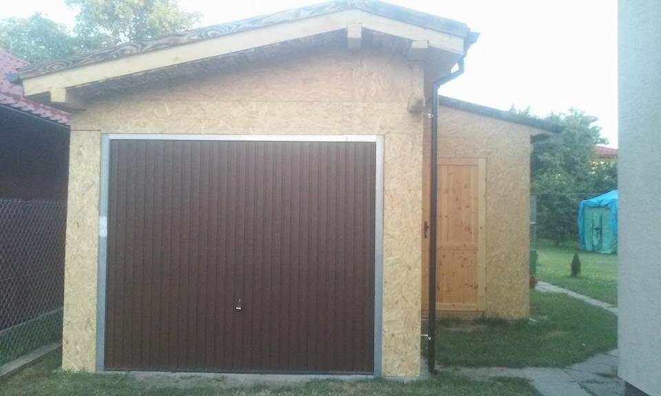 Nowo wybudowany garaż z brązową bramą segmentową i ścianami z płyty OSB, widoczna mała drewniana furtka z boku