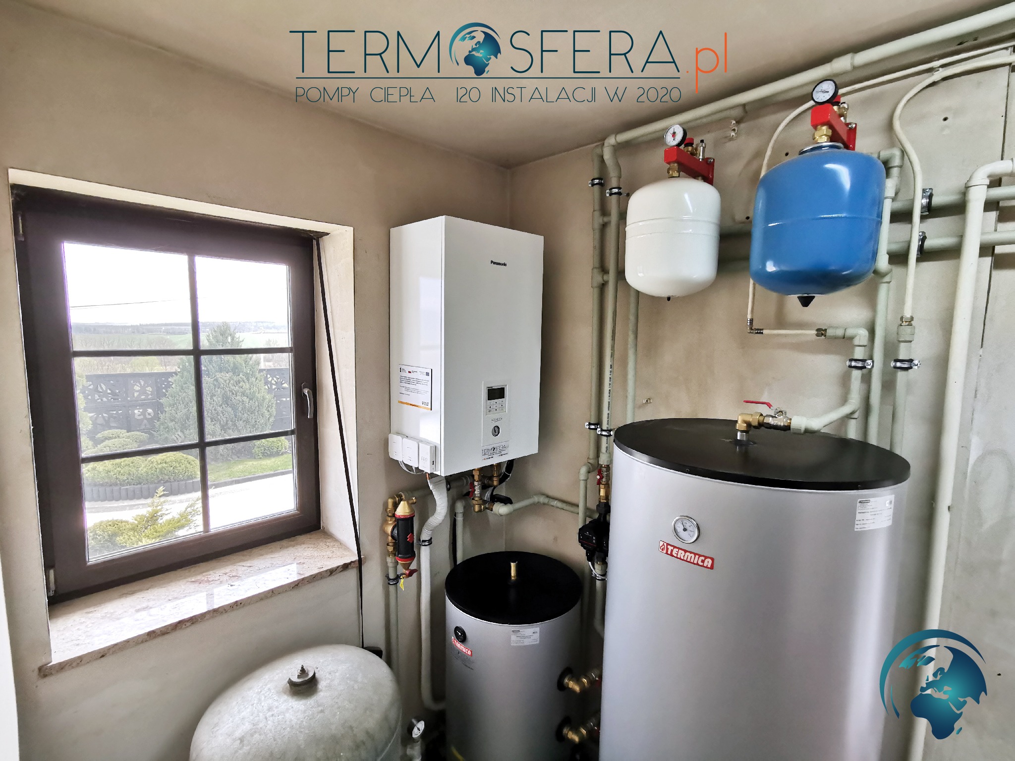 Wnętrze kotłowni z zainstalowaną białą pompą ciepła Panasonic, dwoma srebrnymi zbiornikami Termica, białym i niebieskim zbiornikiem wyrównawczym oraz widokiem na zewnątrz przez okno z marmurowym...