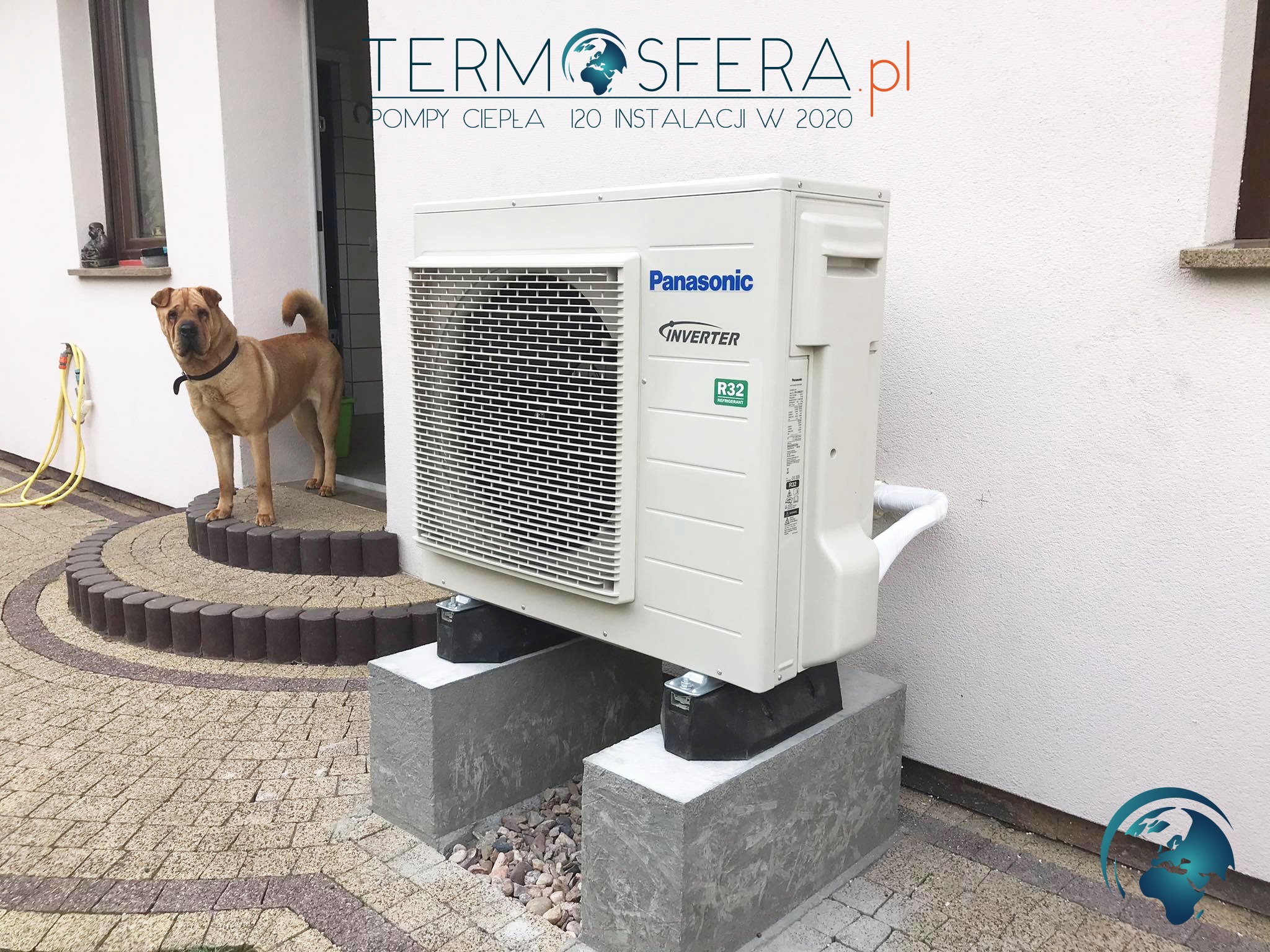 Zewnętrzna jednostka klimatyzacji Panasonic Inverter R32 na betonowych podstawach, przed budynkiem z psem rasy Shar Pei na schodach wejściowych.