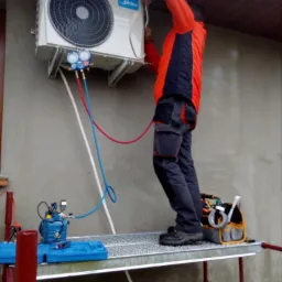 Montaż jednostki zewnętrznej klimatyzatora Midea na elewacji budynku; widoczne manometry i pompa próżniowa na rusztowaniu, instalator w pomarańczowej kurtce.