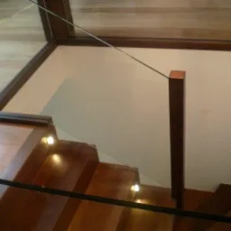 Drewniane schody z podświetleniem stopni i szklaną balustradą, widok z góry, ciemne drewno.