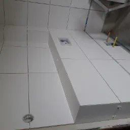 Białe płytki ścienne w trakcie montażu z widocznymi krzyżykami dystansowymi, otwór na puszkę elektryczną i żółte rurki instalacyjne.