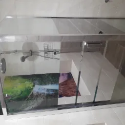 Nowoczesna kabina prysznicowa z chromowanymi elementami i grafiką wodospadu na szklanej ściance, widoczna armatura i półka na kosmetyki.